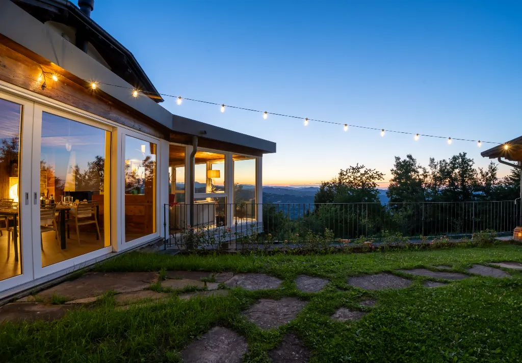 Terrazza panoramica della locanda con grandi vetrate illuminate al tramonto, luci decorative sospese e vista sulle colline e sulla vegetazione circostante.